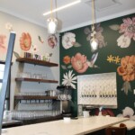 A photo of the interior of a fancy bar with large floral wallpaper and pendant lamps hanging above the bar