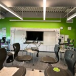 A photo of a classroom interior with bright green walls, gray carpet, and a monitor in the center of the whiteboard