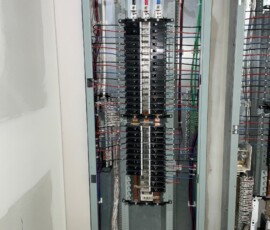 Close-up view of dual vertical electrical breaker panels with detailed wire routing in red, blue, green, and white.