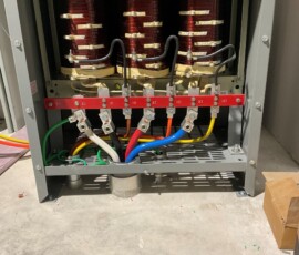 Industrial electrical transformer with brass terminals and colored grounding cables on a concrete floor.
