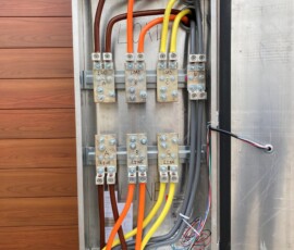 Electrical enclosure with bundled colored cables (orange, yellow, gray) connected to fuse blocks.