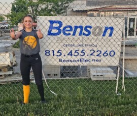 A softball player in front of a Benson construction sign